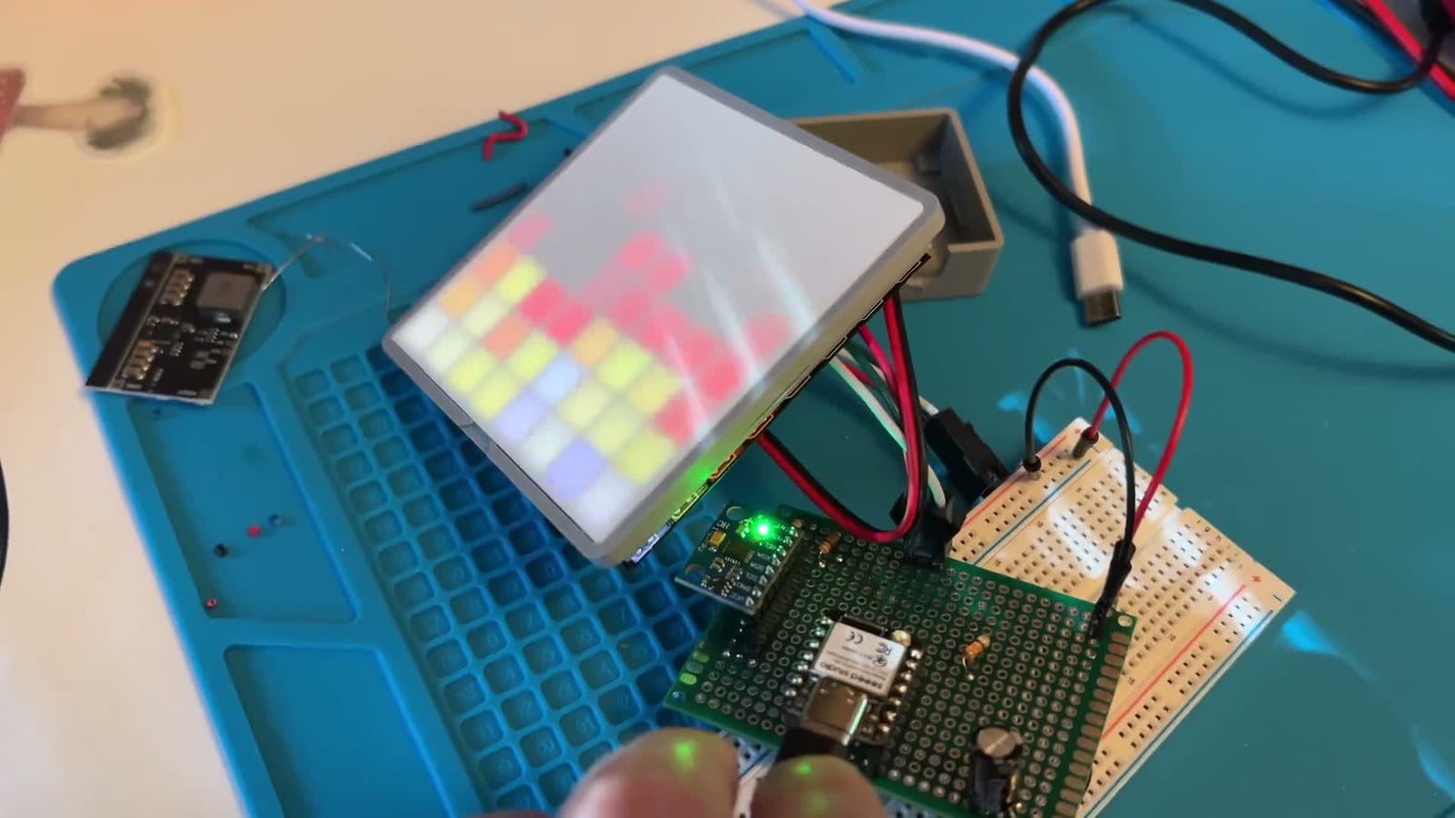 An LED tile on a blue workbench mat behind a white diffuser panel, showing a grid of distinct red, orange and yellow squares rather than individual bright LEDs.