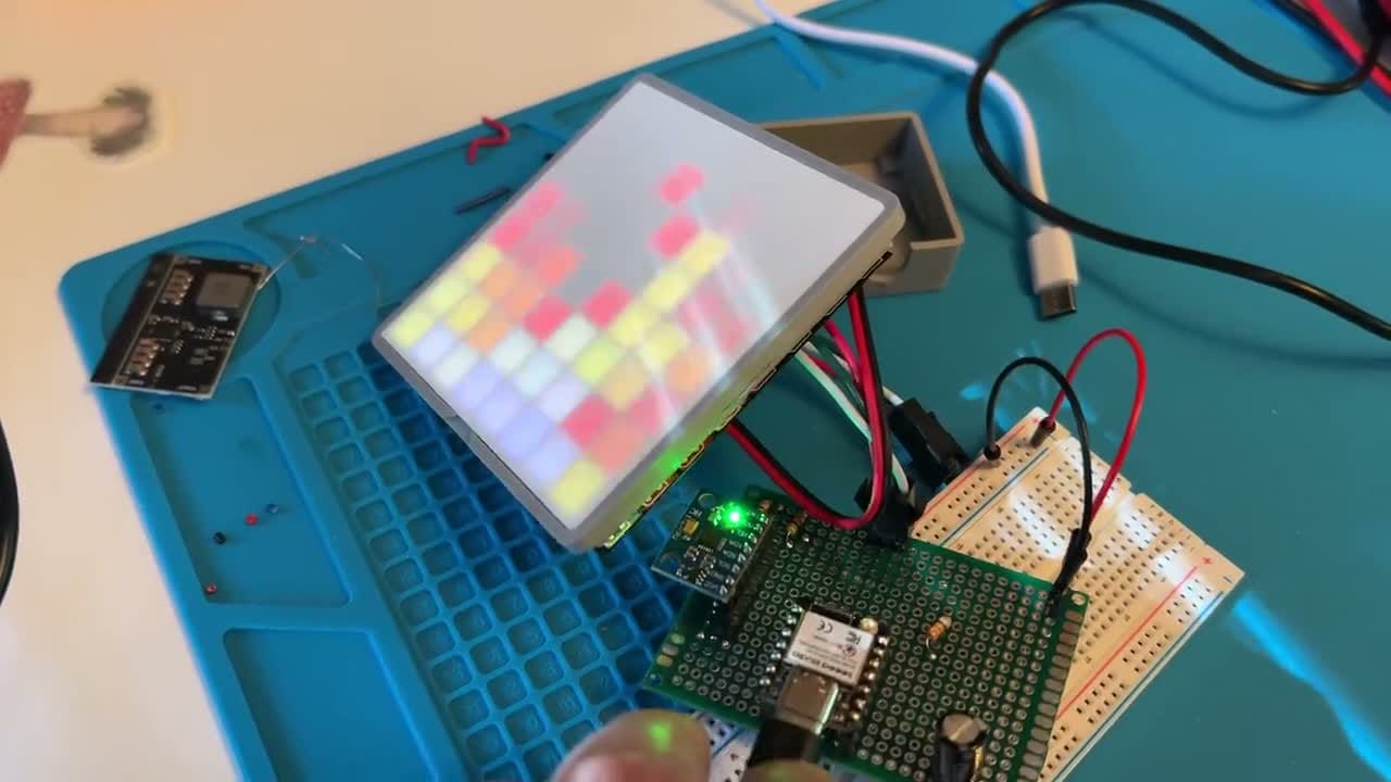 A small addressable-LED matrix panel lit with a shifting grid of colored pixels, wired to an ESP32 on a breadboard.